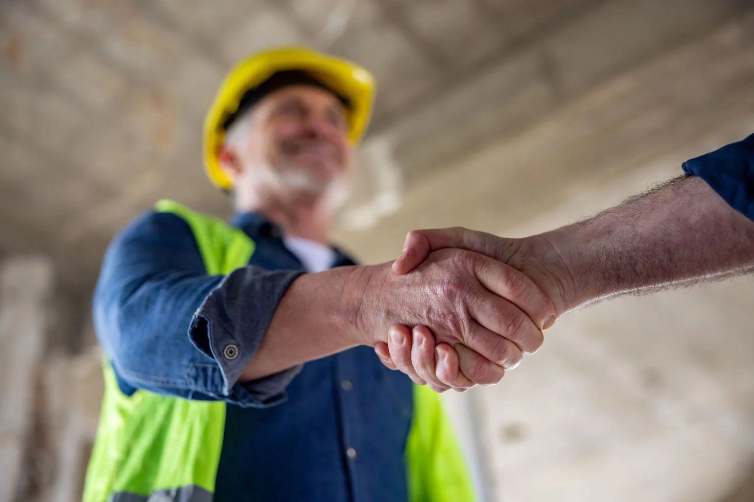Poignée de main entre deux ouvriers du bâtiment sur un chantier, gilet de sécurité jaune.