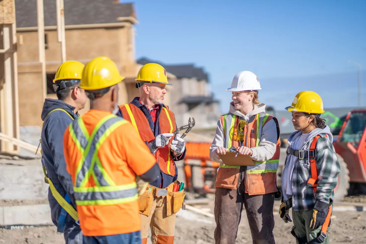 Équipe de chantier en gilets haute visibilité en réunion devant des maisons en construction.
